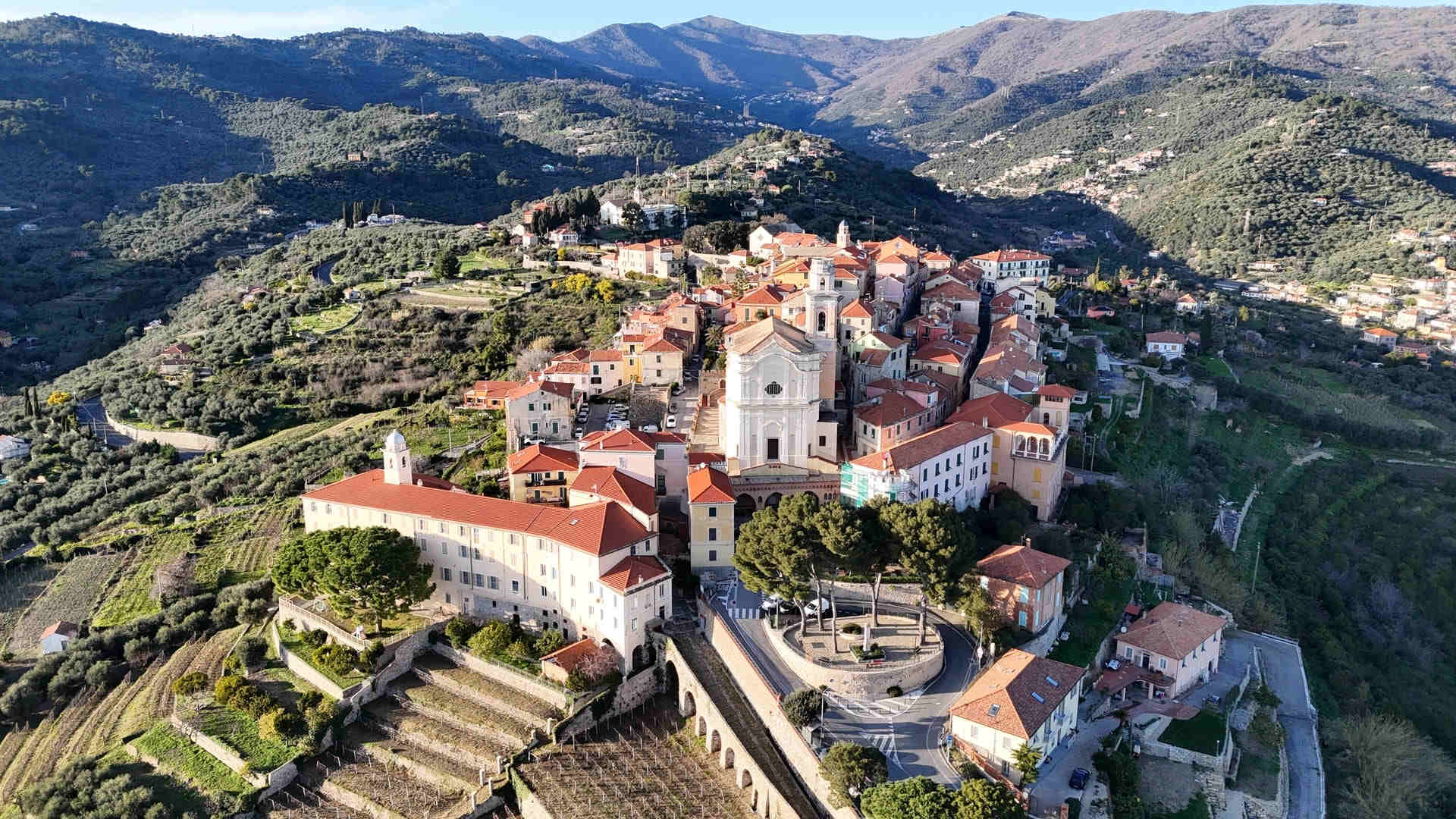 Veduta aerea del borgo medievale di Diano Castello arroccato sulla collina tra uliveti, con la chiesa barocca e i tetti in cotto, entroterra di Diano Marina